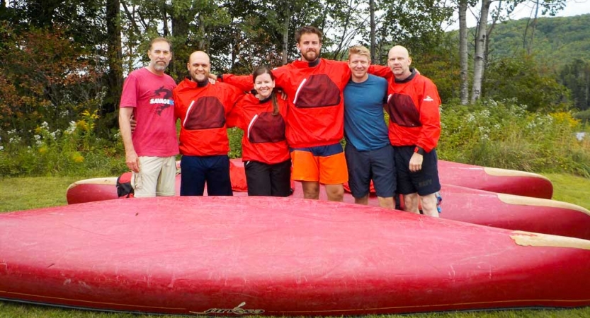 a group of veterans with their arms around each other smile at the camera while standing between canoes